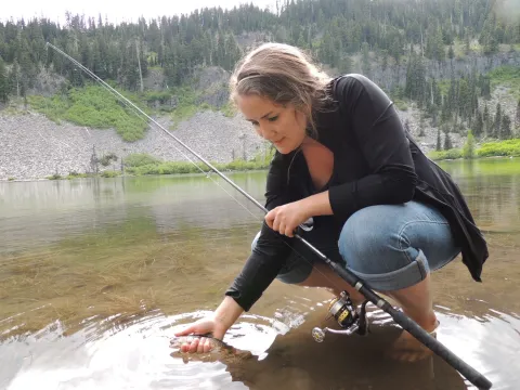Girl catching mountain trout in alpine lake