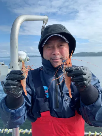 Mark Yuasa holding up two shrimp, one in each hand.